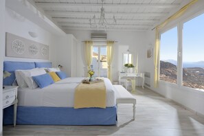 A bedroom with a large bed, a bedside table, a desk, and a view of the landscape.