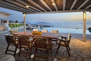 A covered outdoor dining area with a table and chairs, overlooking a sea view.