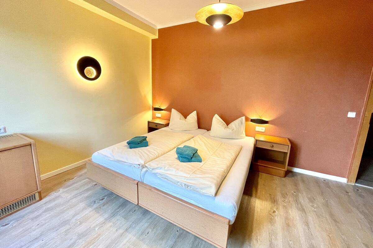 Una camera d'albergo con un letto, comodini e una lampada a sospensione.