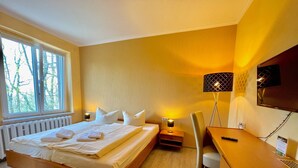 A bedroom with a bed, bedside tables, a desk, a chair, a lamp, and a TV.