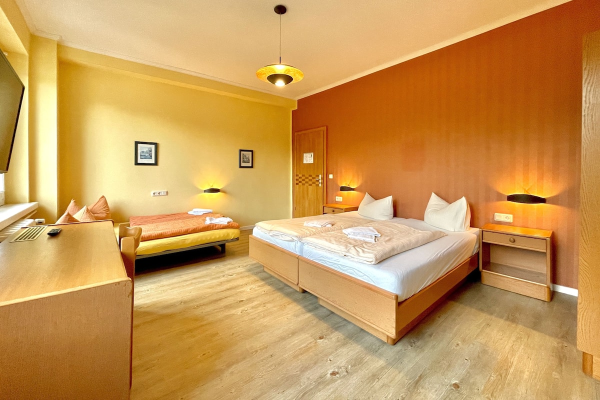 Una camera d'albergo con un letto grande, un letto più piccolo, una scrivania e una sedia.