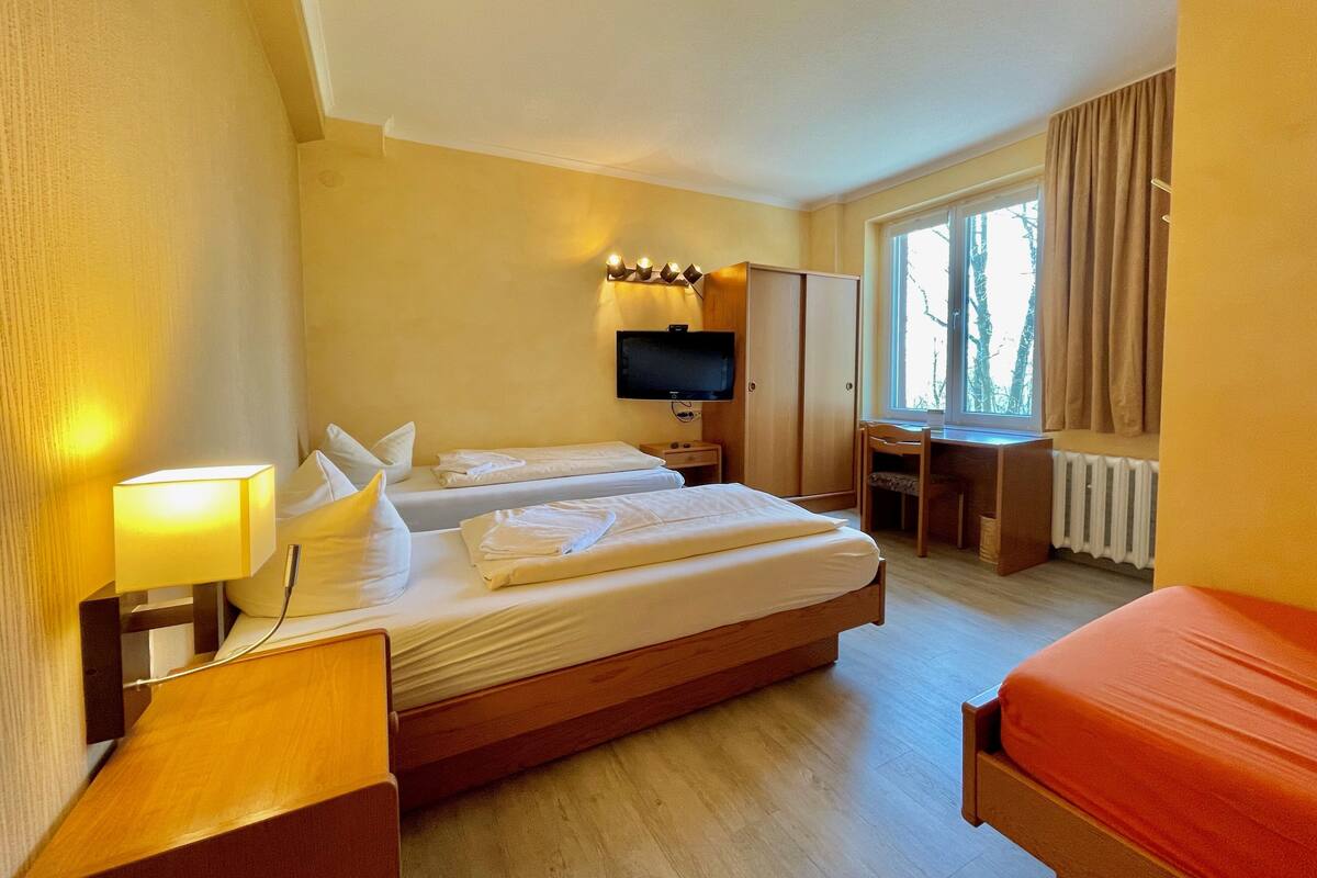 Camera d'albergo con due letti singoli, una scrivania, una sedia, una televisione e una finestra con tende.