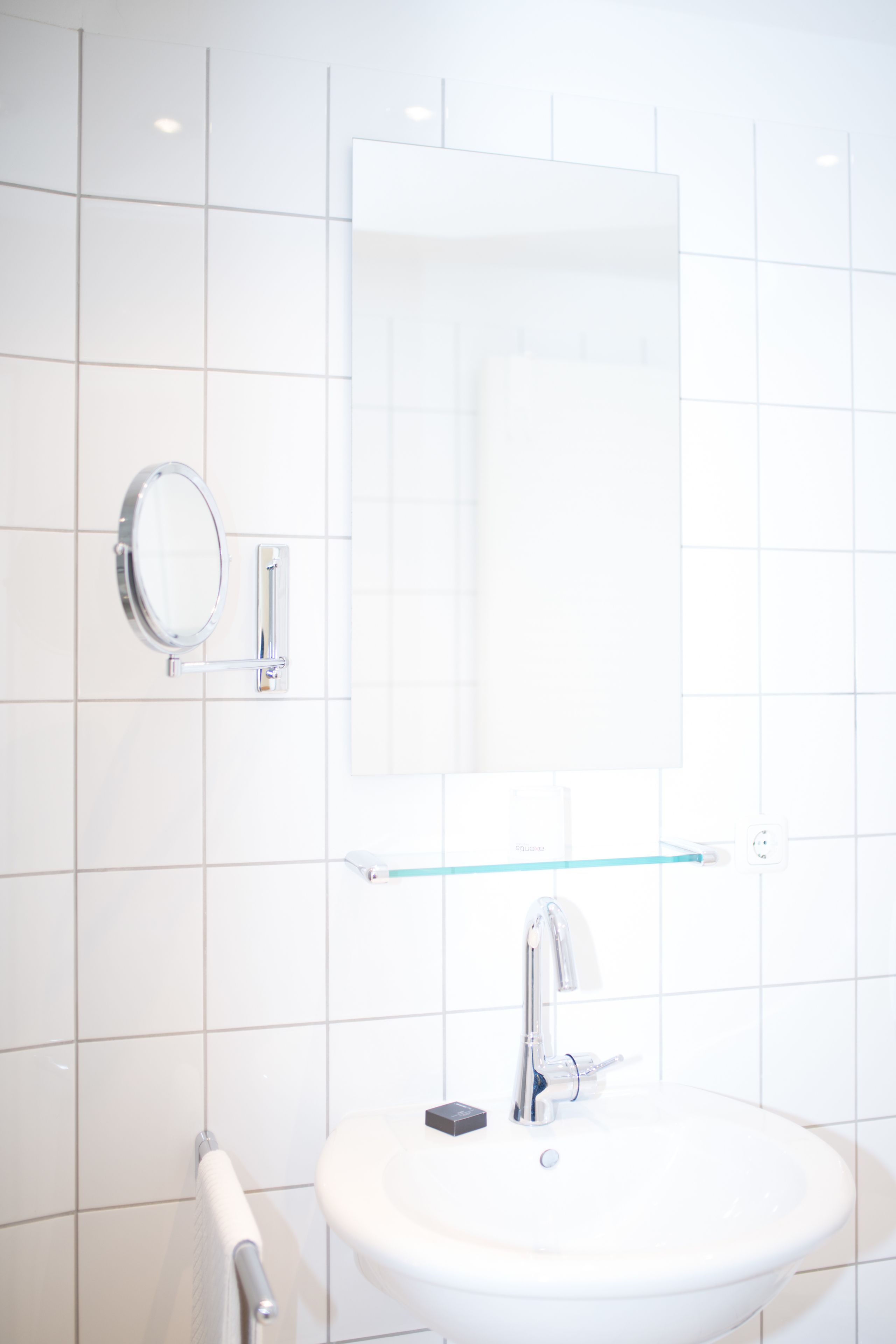 Un baño con un lavamanos blanco, un espejo y un estante de vidrio.