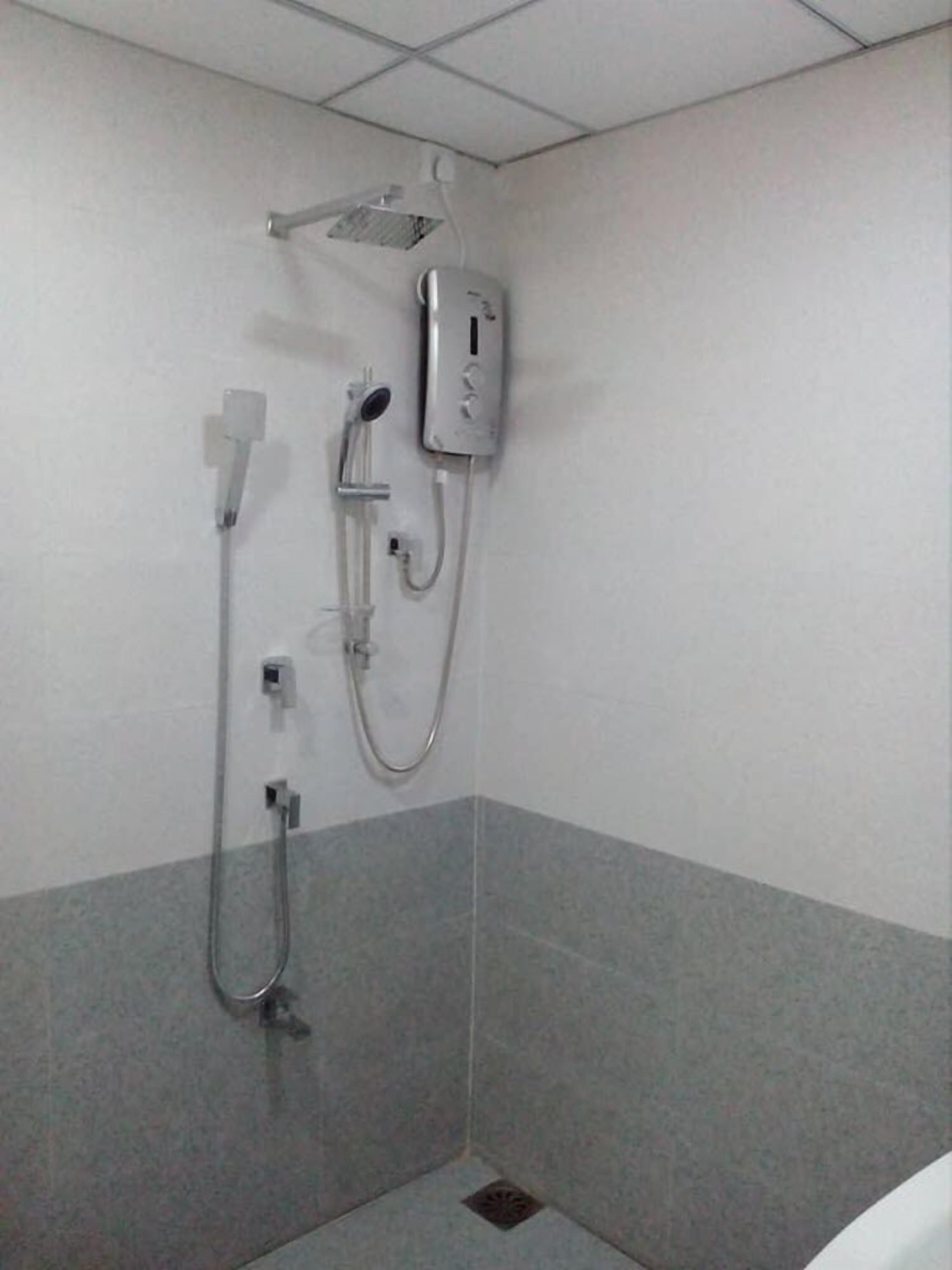 Un espace douche équipé d’un pommeau de douche à main, d’un robinet mural et d’un panneau de commande.