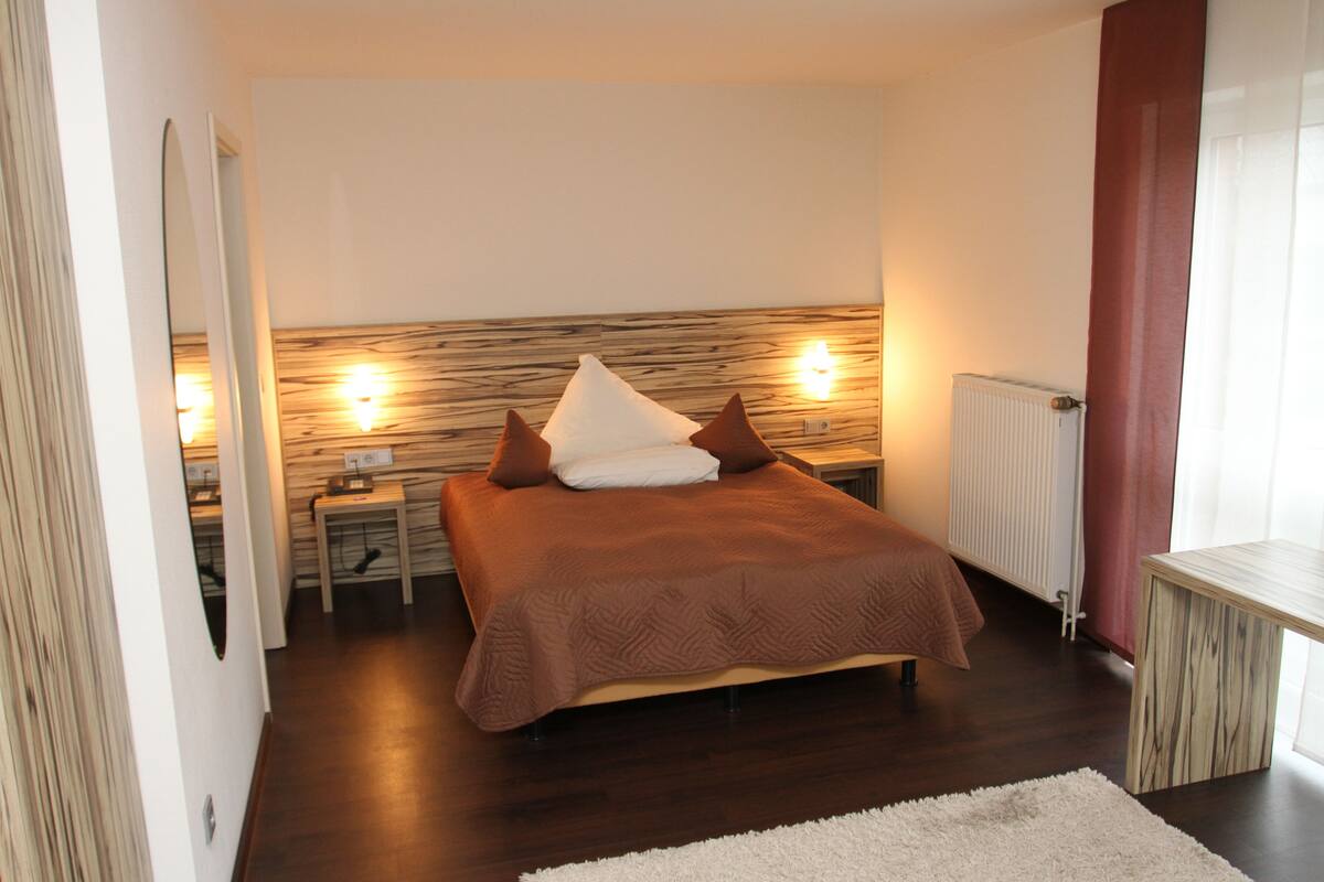 A bedroom with a bed, bedside tables, a radiator, and a mirror.