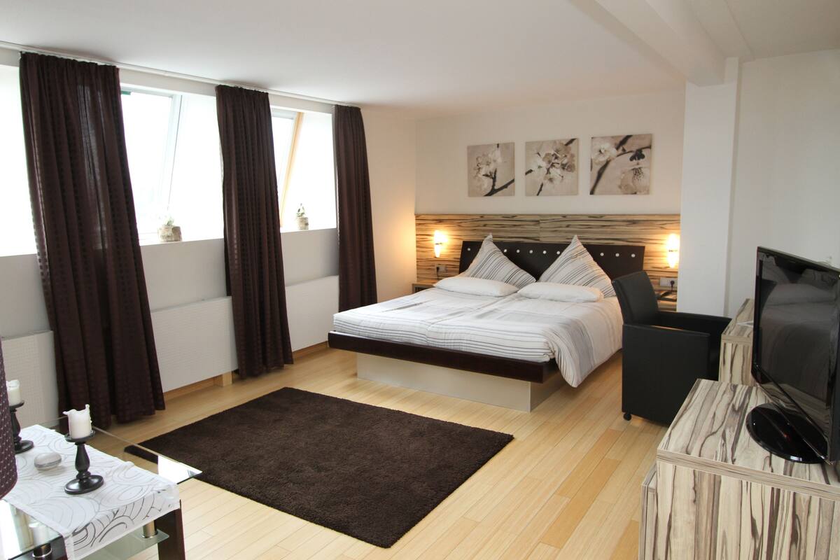 A modern bedroom with a large bed, bedside tables, a flat-screen TV, and artwork on the wall.