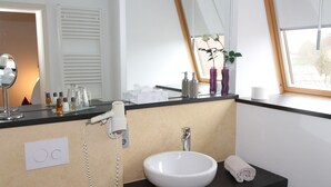 A modern bathroom with a large mirror, a white sink, a hairdryer, and toiletries on the counter. - Designhotel Im Südfeld (Kamen)