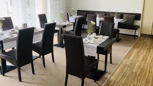 A dining area with multiple tables and chairs, a wooden floor, and a painting on the wall. - Designhotel Im Südfeld (Kamen)