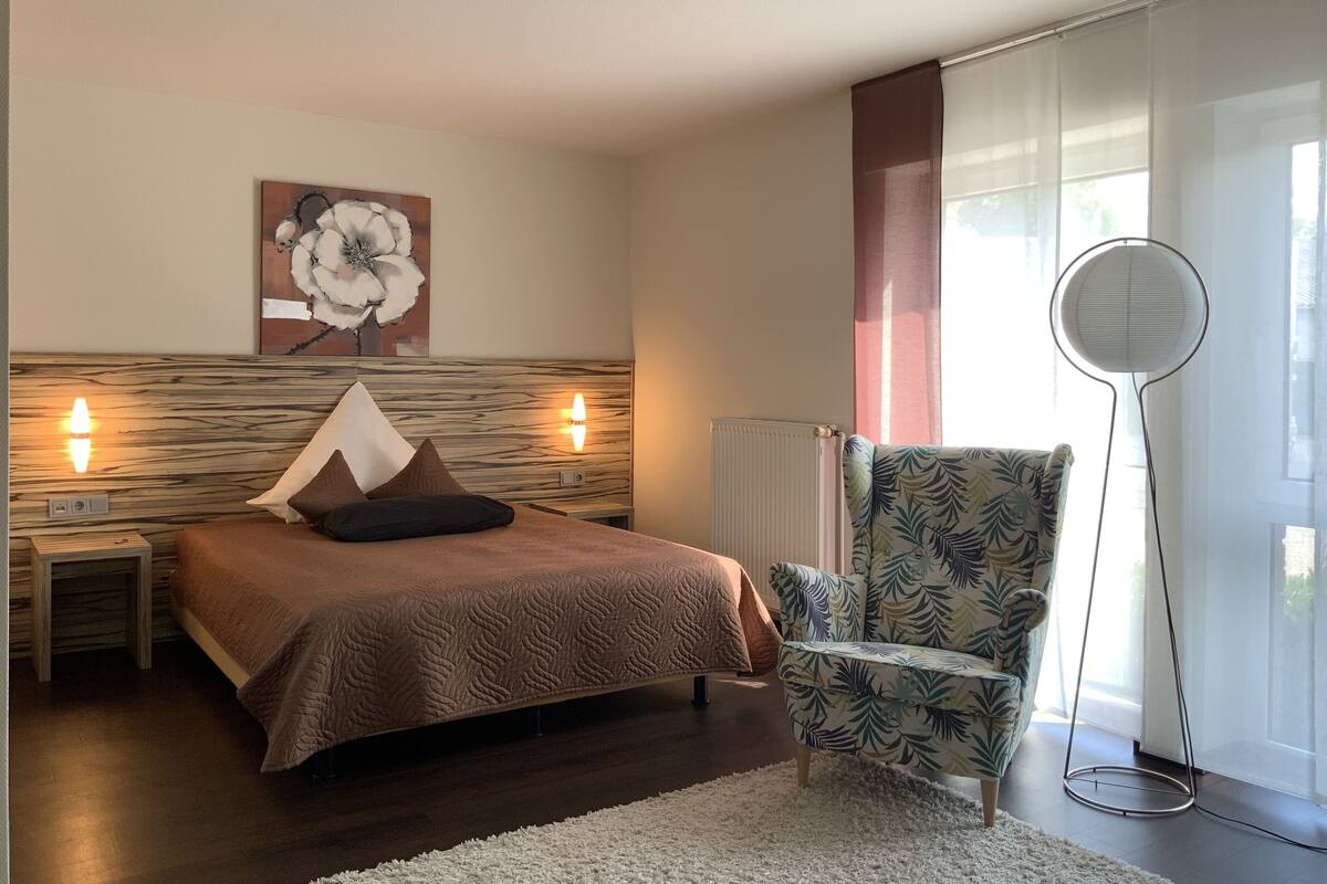 A bedroom with a bed, a chair, a radiator, and a window with curtains.