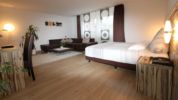 A modern bedroom with a large bed, a sofa, a coffee table, and a desk with a lamp. - Designhotel Im Südfeld (Kamen)