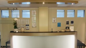 A reception desk with a lighted front, framed certificates on the wall, and a potted plant. - Designhotel Im Südfeld (Kamen)