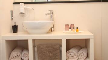 A modern bathroom with a white sink, mirror, and shelves for towels.