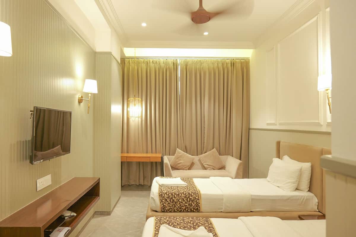 Habitación de hotel con dos camas, televisión, escritorio y ventana con cortinas.