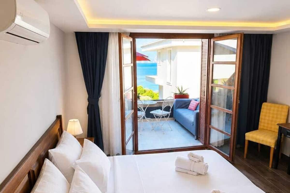 Quarto de hotel com cama, mesa de cabeceira, luminária, vista para o exterior e varanda com mobiliário.