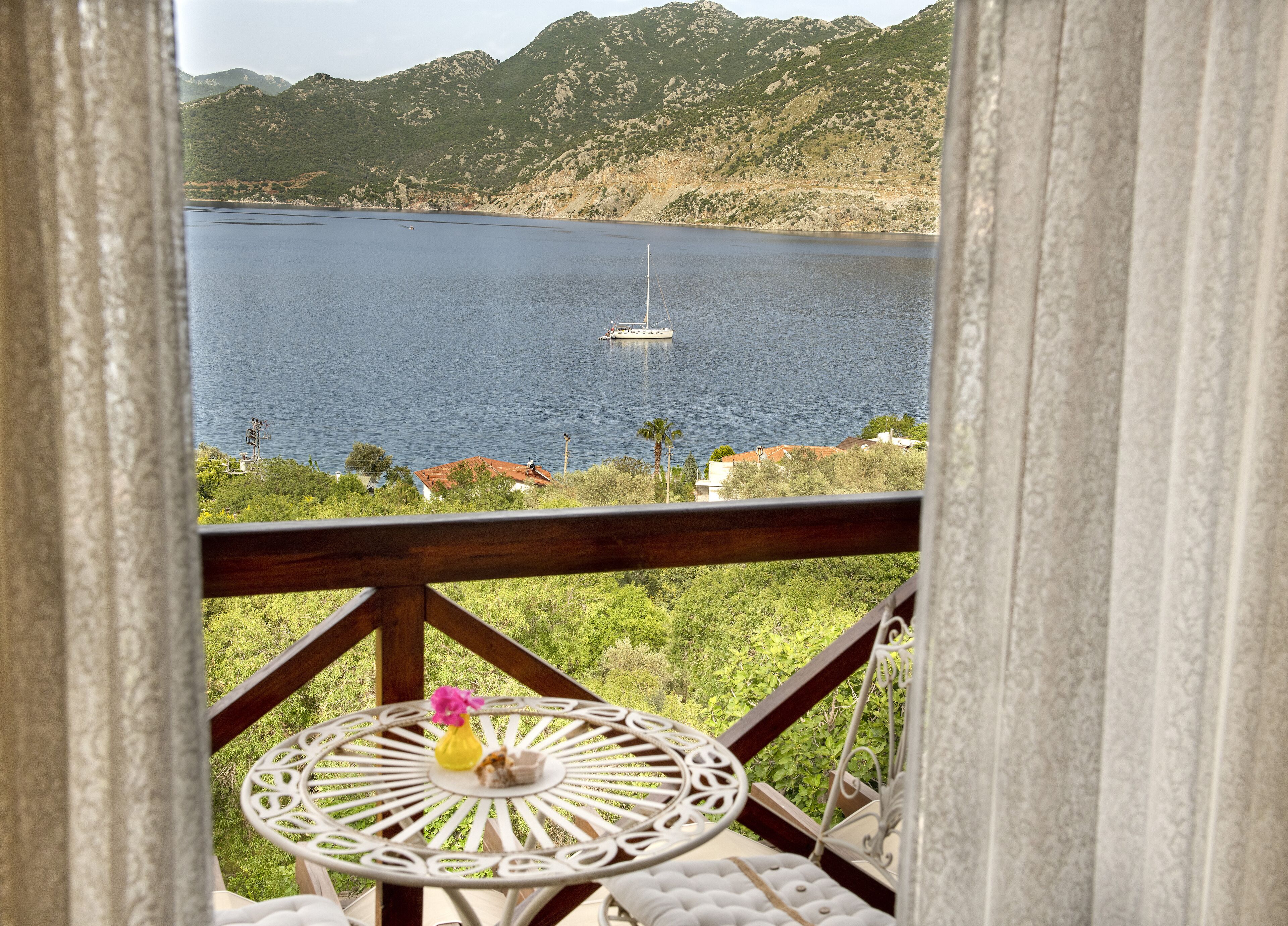 A balcony with a view of a lake, a boat, and mountains in the background.