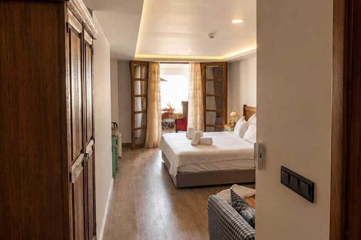 Quarto de hotel com cama, um espaço de estar pequeno e um guarda-roupa de madeira.