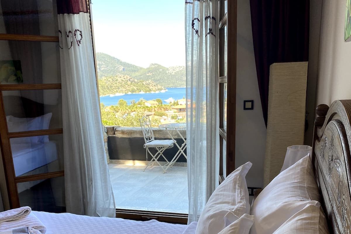 Quarto de hotel com cama, vista para o mar e varanda com uma cadeira.