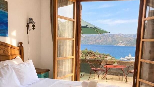 Ett hotellrum med en säng, utsikt över havet och ett bord med stolar på uteplatsen.