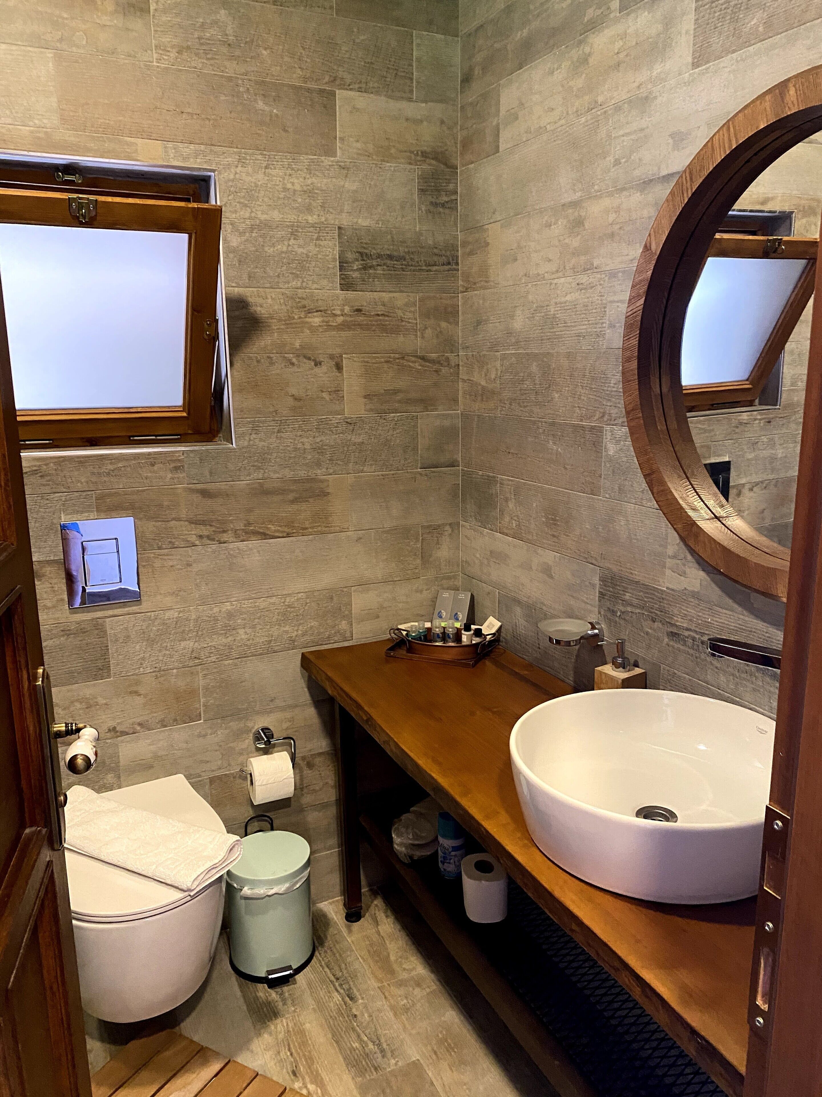 Un bagno con un mobile vanitario in legno, un ampio specchio rotondo e un lavandino bianco.