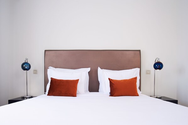 A neatly made bed with white and orange pillows, a brown headboard, and two modern lamps on either side.