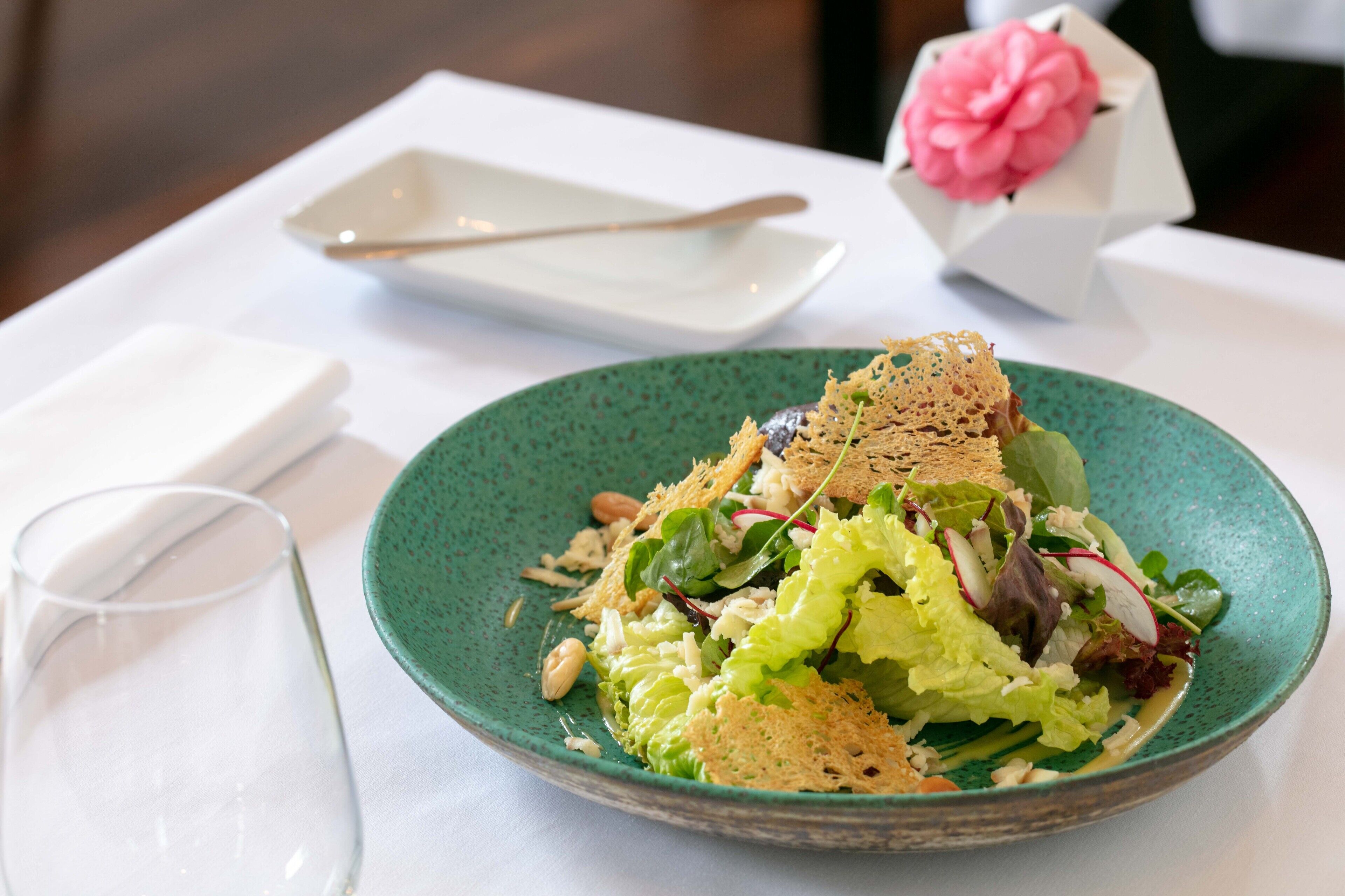 Un plato de ensalada con crutones y nueces, un vaso de agua y una servilleta blanca sobre una mesa.