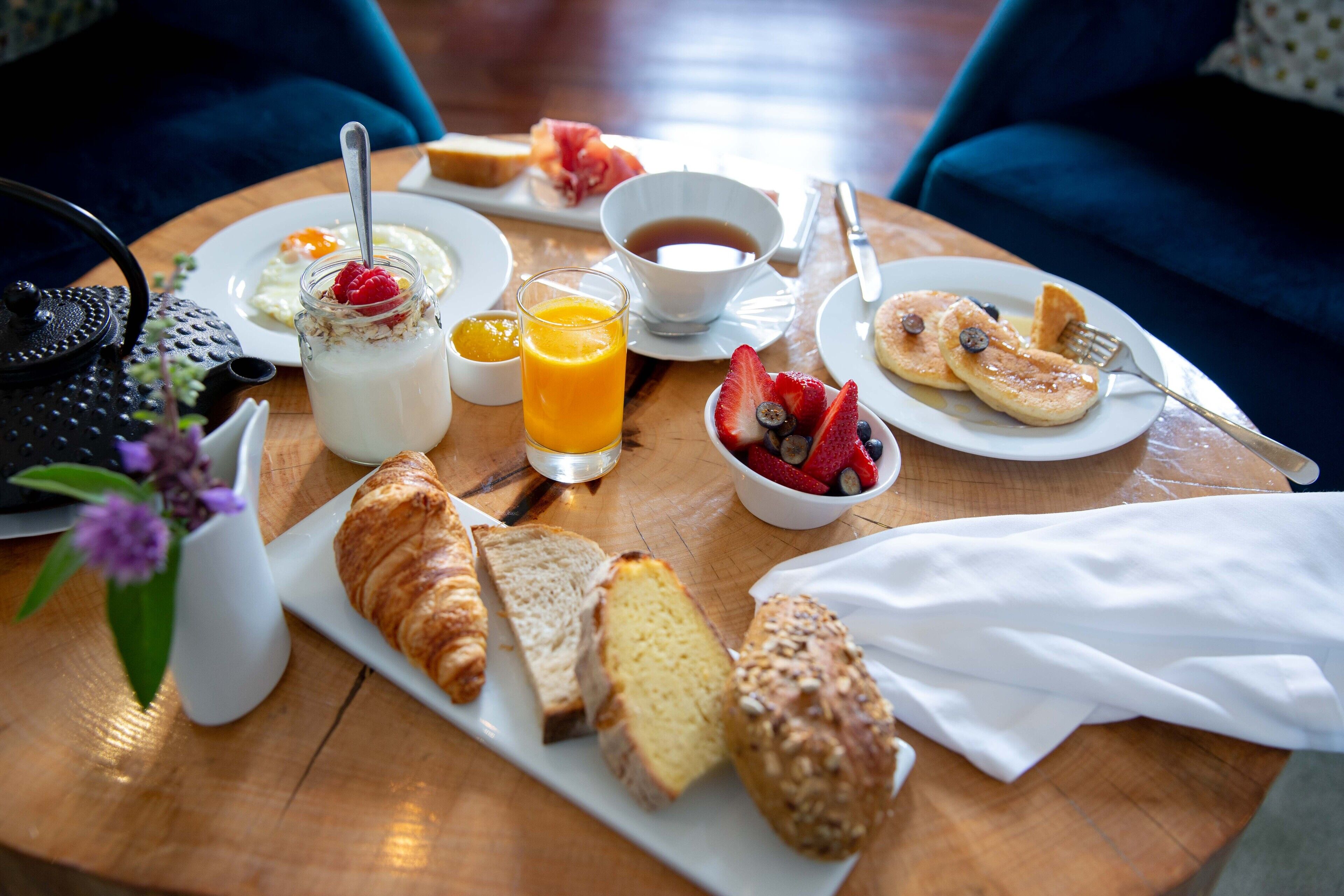 Une table de petit-déjeuner avec des croissants, du pain, des fruits, un verre de jus d’orange et une tasse de café.