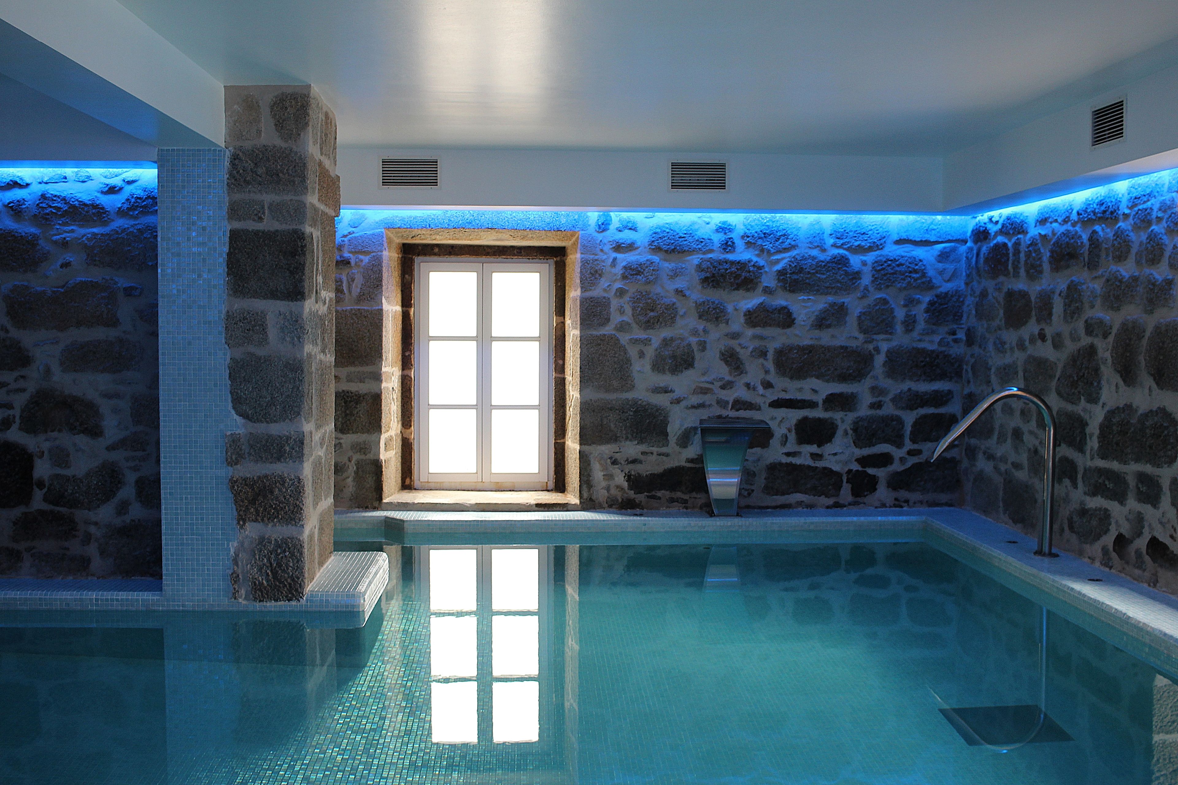 A stone-walled indoor pool with a clear glass bottom, a window, and a metal faucet.