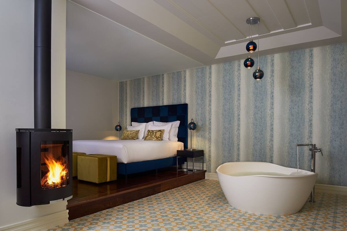 A modern bedroom with a large bed, a fireplace, a bathtub, and a nightstand with lamps.