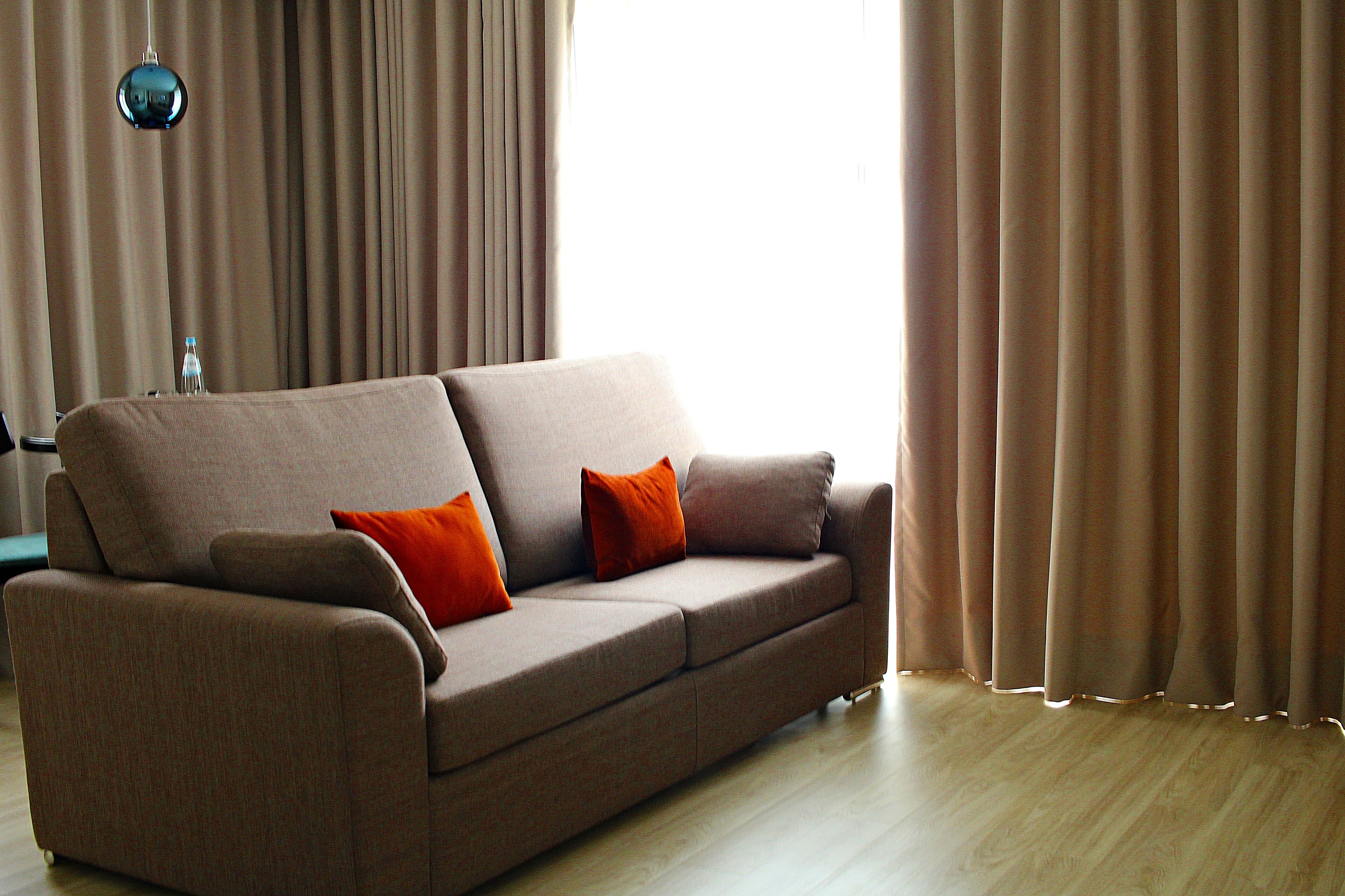 A modern living room with a beige sofa, two orange cushions, and a blue pendant light.