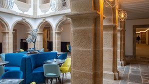 Amplio espacio interior con columnas de piedra, asientos azules y amarillos, y lámparas colgantes.