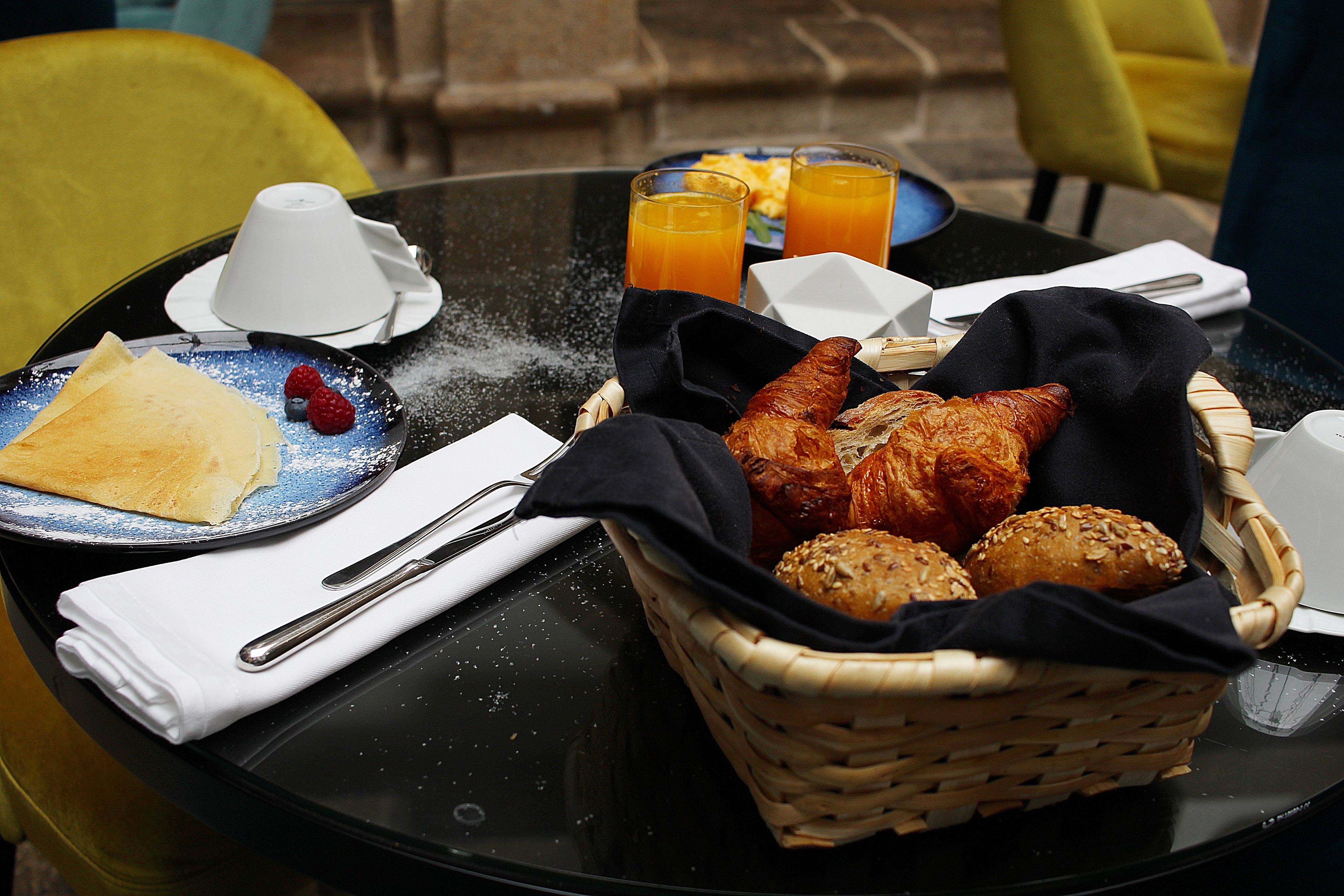 A breakfast table with croissants, bread rolls, and a basket of bread.