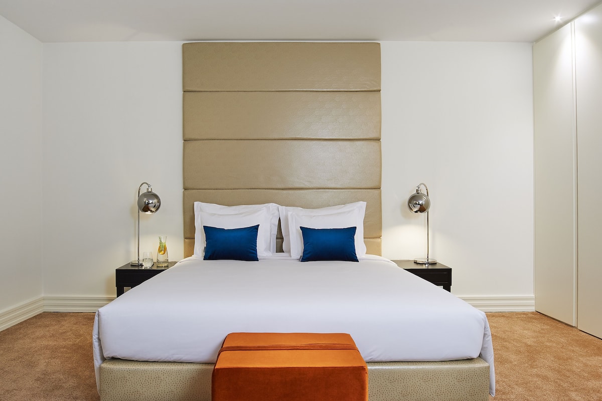 A neatly made bed with white and blue bedding, two bedside tables with lamps, and a brown carpeted floor.