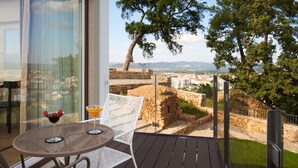 Un balcón con mesa y sillas, vistas a una pared de piedra histórica y un árbol.