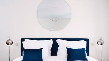 Habitación de hotel con una cama grande, dos lámparas de noche, un espejo redondo en la pared y un cabecero azul.