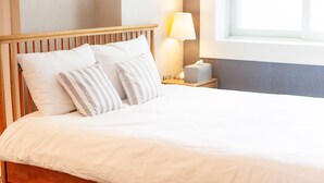 A neatly made bed with white bedding and striped pillows, a bedside lamp, and a tissue box on a wooden nightstand. - MIHOJAE Hostel Busan (Busan)