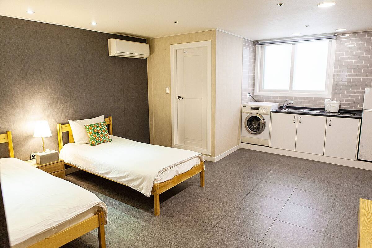 Une chambre d’hôtel compacte avec deux lits simples, un lave-linge et une petite kitchenette.