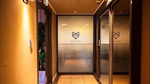 A hallway with a glass door leading to a lounge area, featuring a logo and the name 'MIHOJAE'. - MIHOJAE Hostel Busan (Busan)