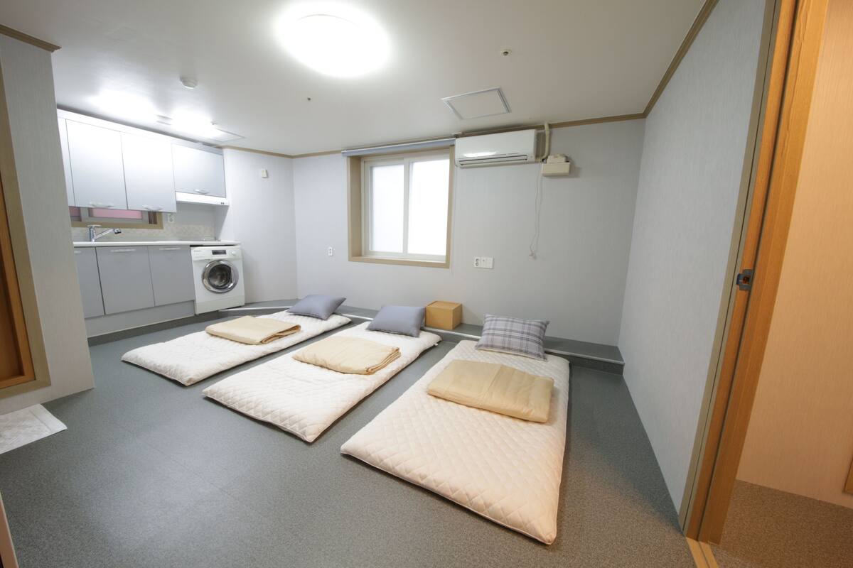 Une petite pièce comprenant deux lits, un lave-linge, une fenêtre et un coin cuisine.