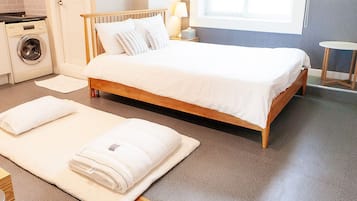A bedroom with a bed for three people, a washing machine, a small table, and a lamp.