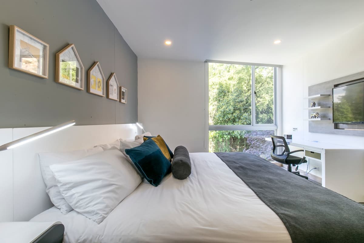 A modern bedroom with a large bed, a desk, and a television.
