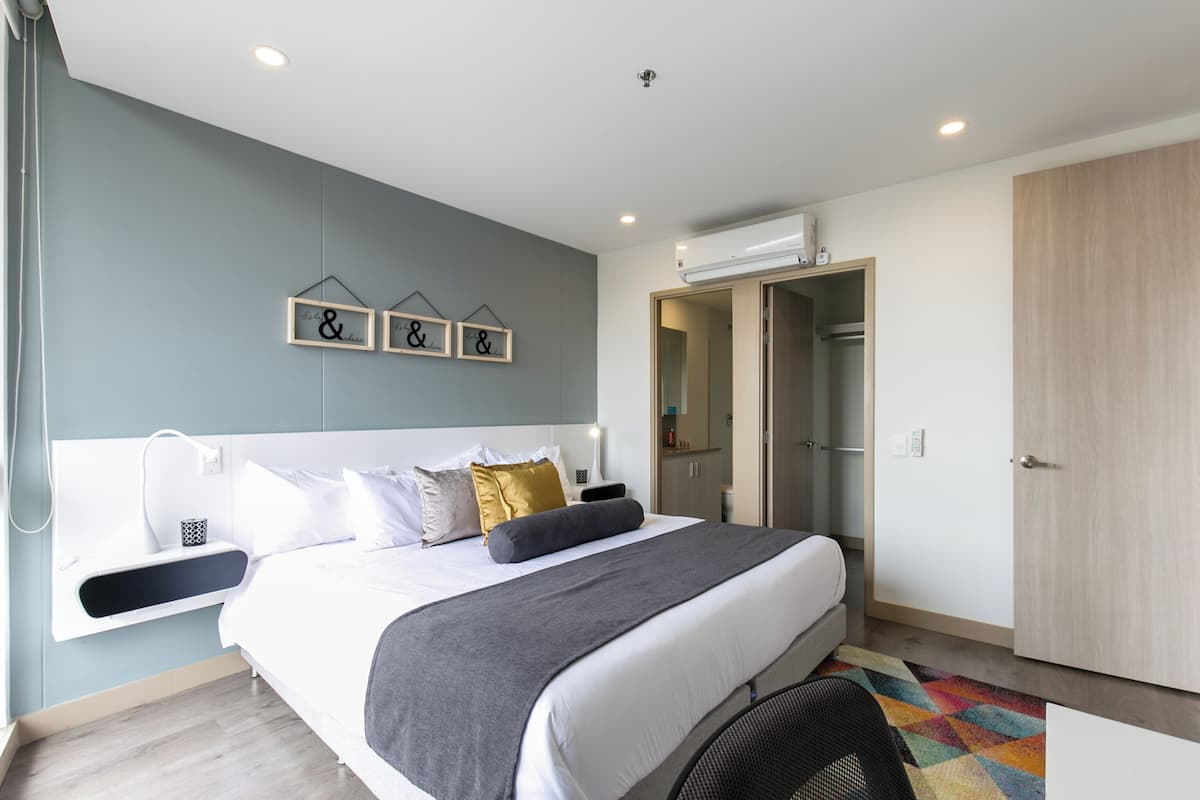 A modern bedroom with a large bed, a bedside table, a wardrobe, and a wall-mounted shelf.