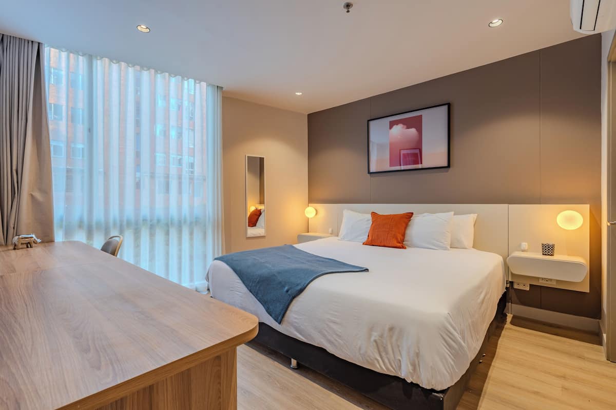 A hotel room with a large bed, bedside tables, a desk, and a window with curtains.