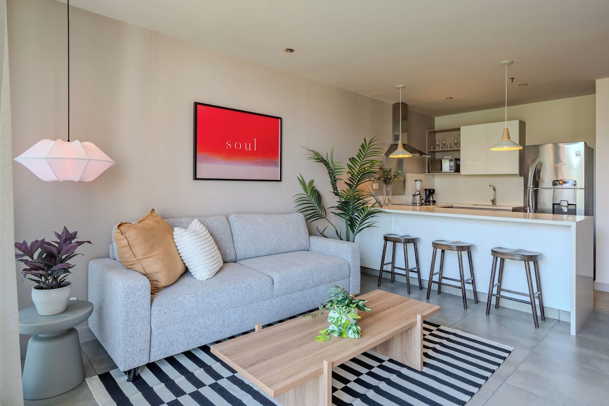 A modern living room with a grey sofa, a coffee table, and a kitchen area with bar stools.