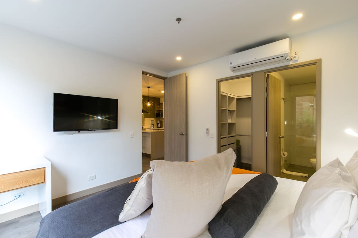A modern hotel room with a bed, a TV mounted on the wall, and an air conditioning unit.