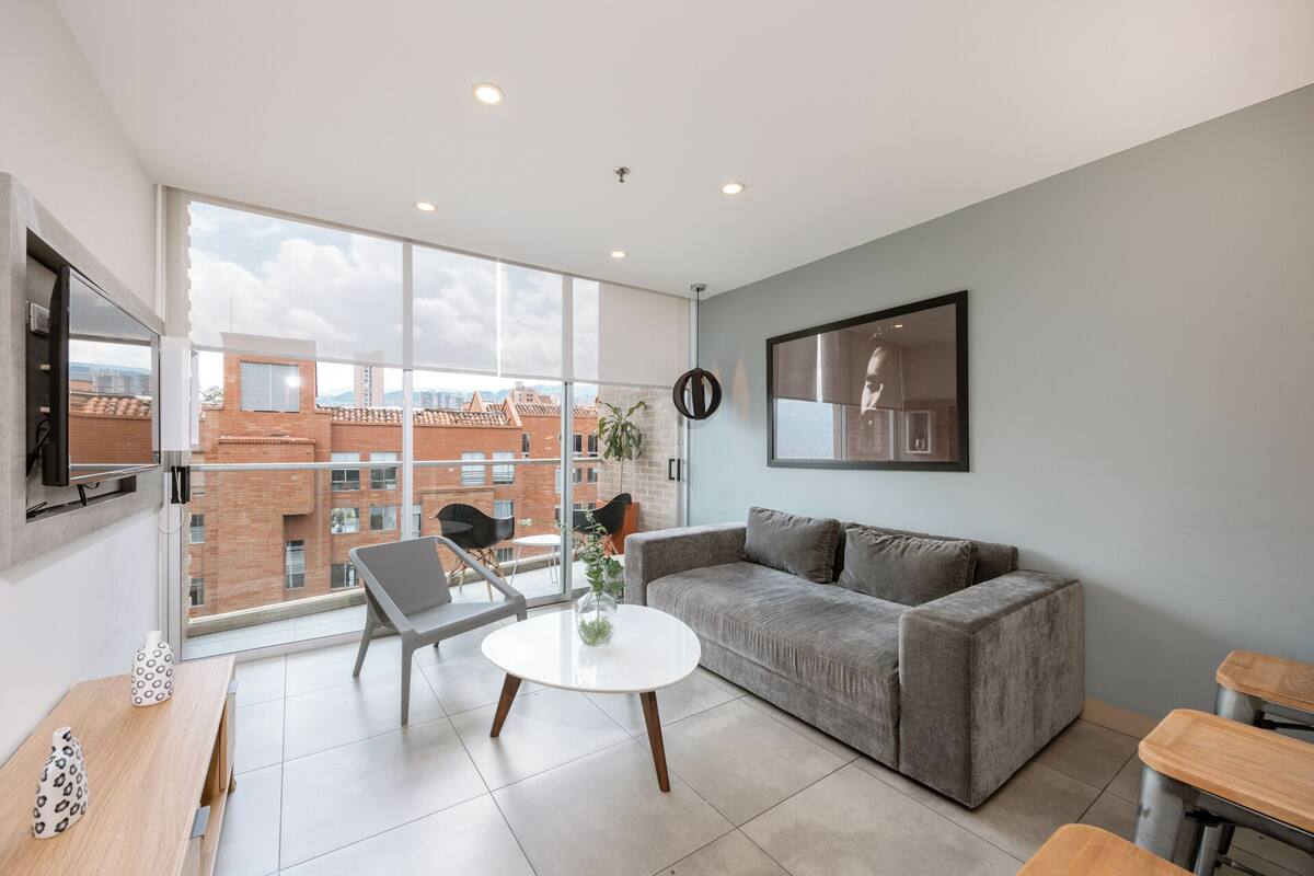A modern living room with a grey sofa, a round white coffee table, and a TV mounted on the wall.