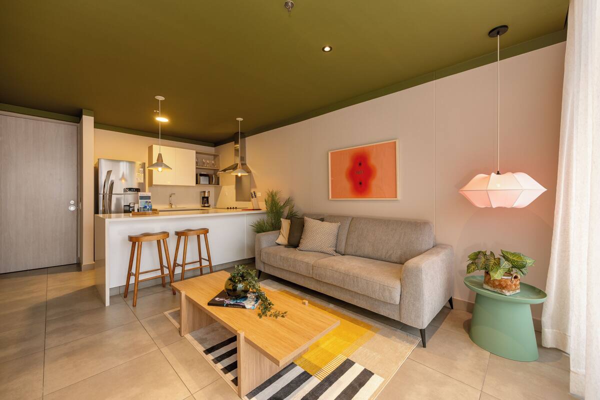 A modern living space with a kitchen, a sofa, a coffee table, and a small side table with a plant.