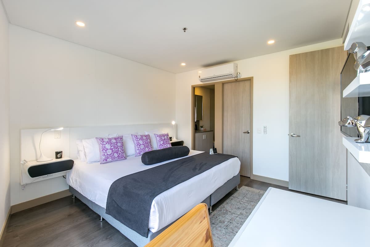 A modern bedroom with a bed, bedside tables, a wardrobe, and an air conditioning unit.