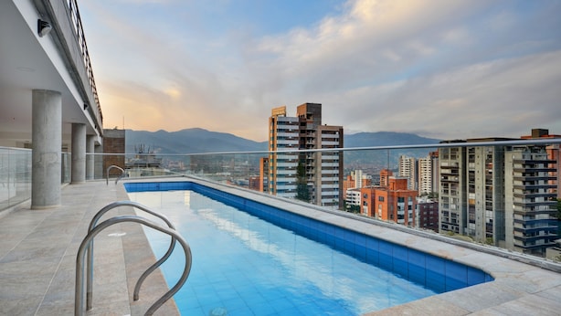 Una piscina en la azotea con vistas a edificios altos y montañas al fondo.