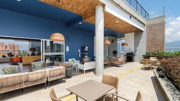 Un lounge en la azotea con asientos, mesas y vistas panorámicas de la ciudad.