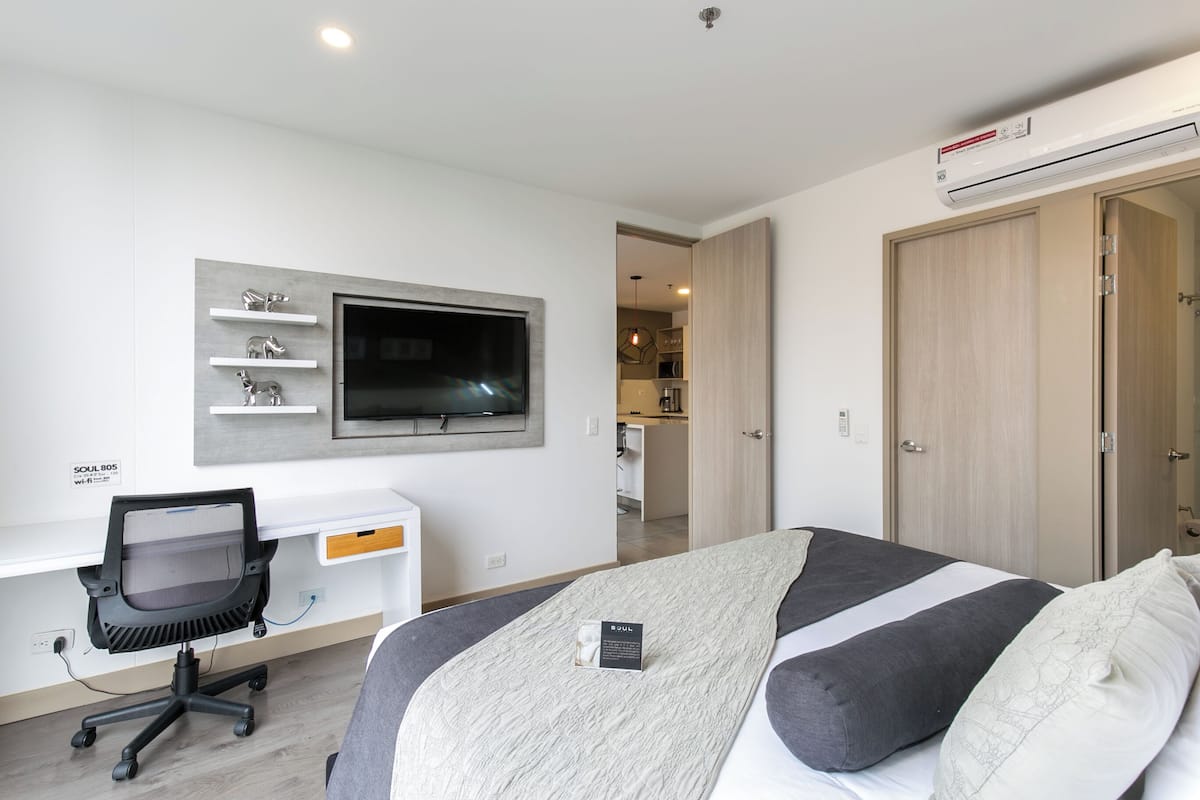 A modern hotel room with a bed, a desk with a computer, a TV, and a wardrobe.